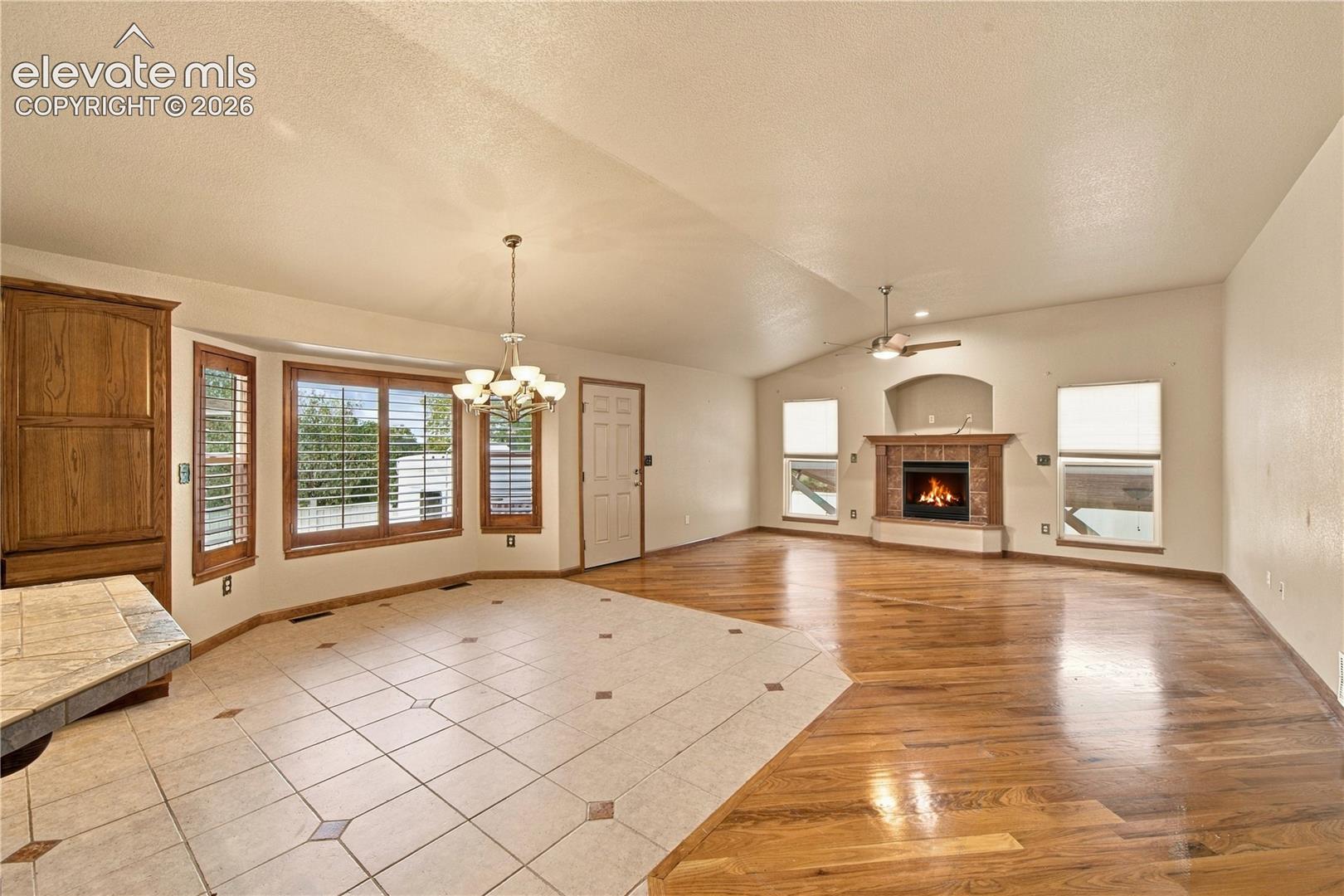 Open-concept room featuring wood-finish flooring, ceramic tile flooring inlay, a fireplace with a masonry surround and arched niche, and a multi-pane bay window