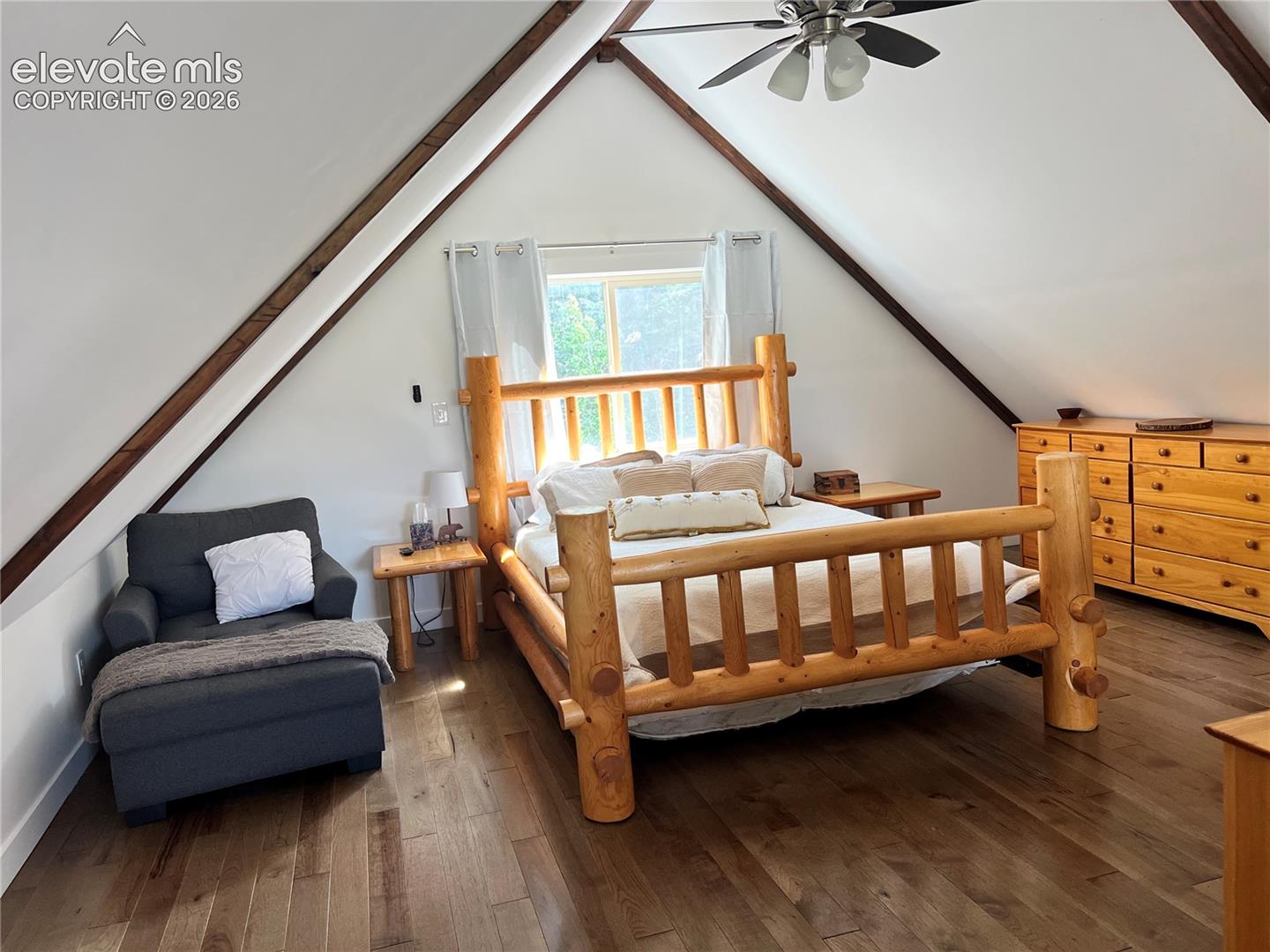 Vaulted ceiling with exposed wood beams, wood-finish flooring, and a ceiling fan with integrated lighting