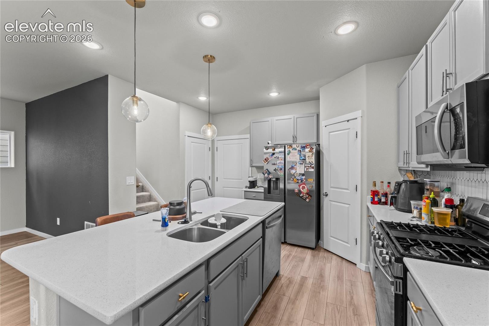 Kitchen featuring a spacious island with dual sinks, light-toned countertops, pendant lighting, and wood-finish flooring