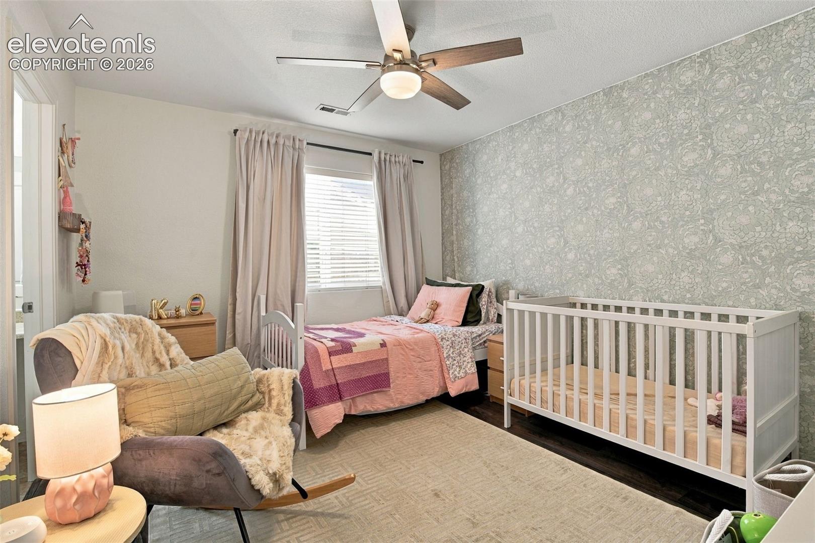 Patterned accent wall, window with blinds, ceiling fan with integrated lighting, wood-finish flooring, and recessed lighting