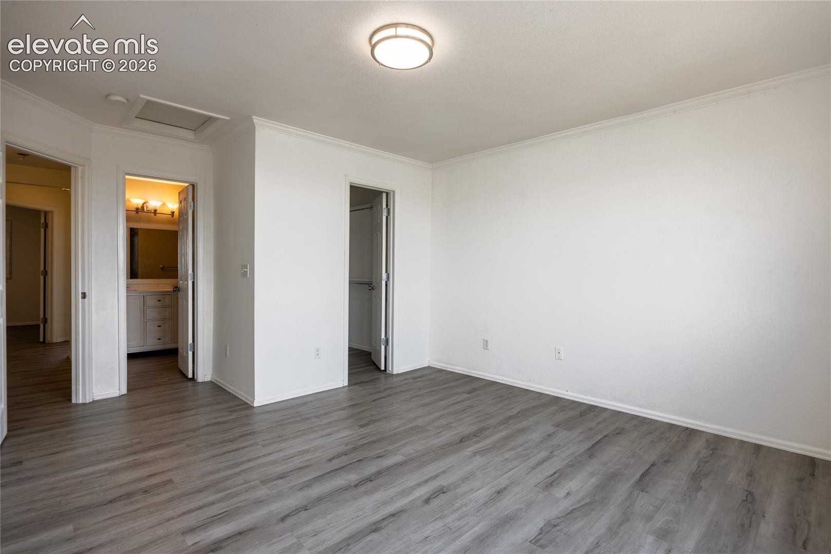 Spacious room with wood-finish flooring, crown molding, and a flush mount ceiling light