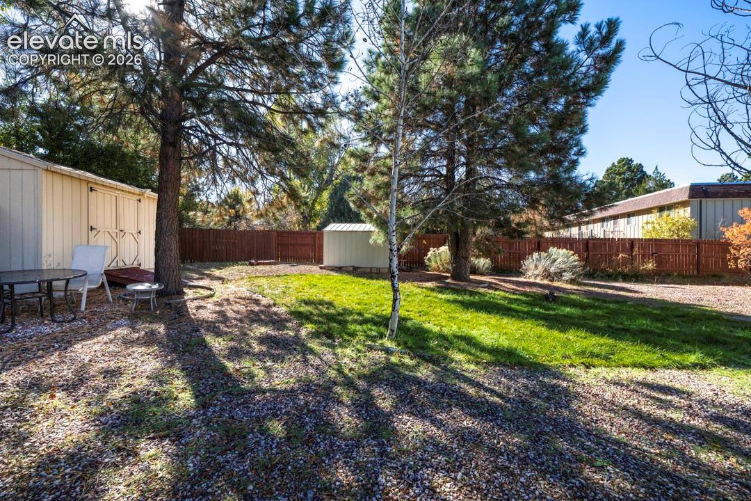 Backyard featuring a grass lawn, mature trees, wood privacy fencing, and two storage structures