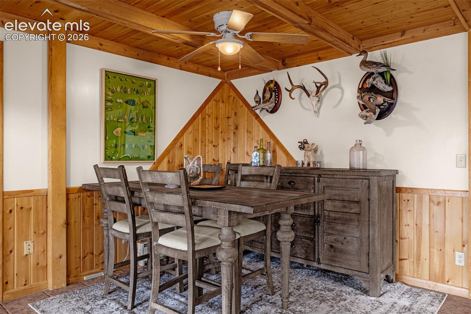 Wood-paneled ceiling with exposed beams, wood-paneled wainscoting, and a central ceiling fan with integrated lighting