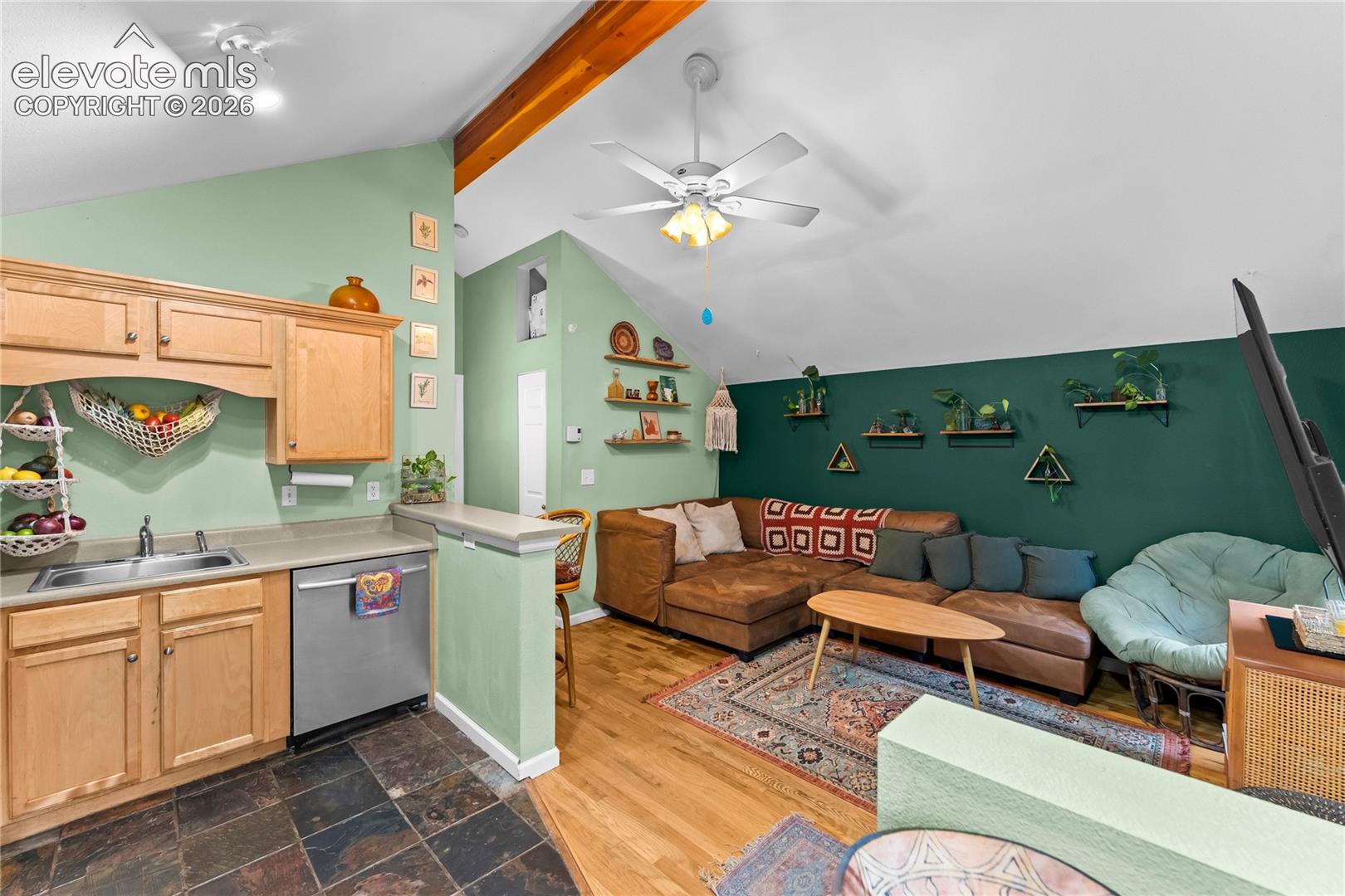 Vaulted ceilings with exposed timber beam, wood-finish flooring, stone-tile flooring, and ceiling fan with integrated lighting