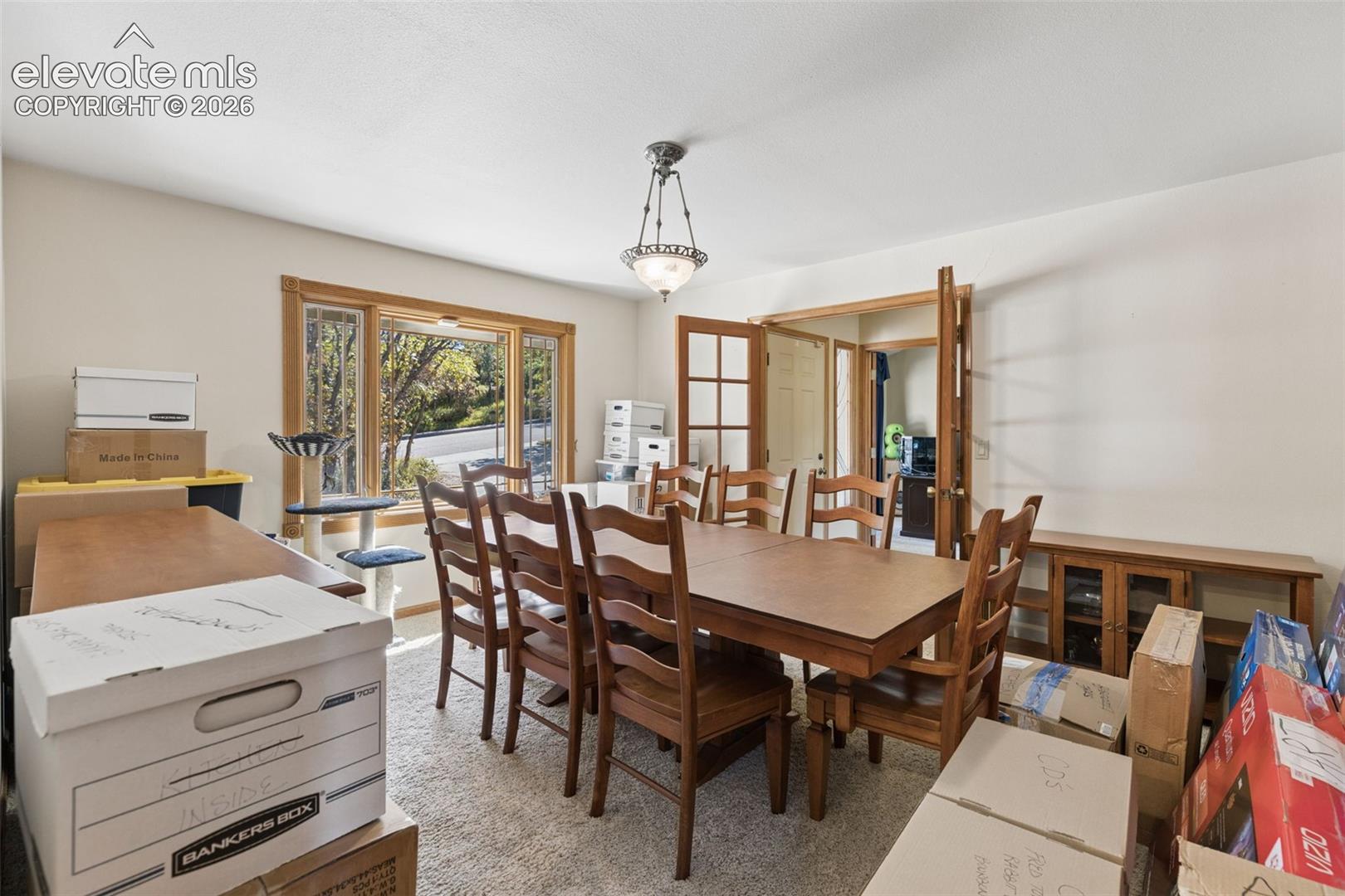 Dining area featuring large window with wood trim, decorative hanging light fixture, and wooden French doors
