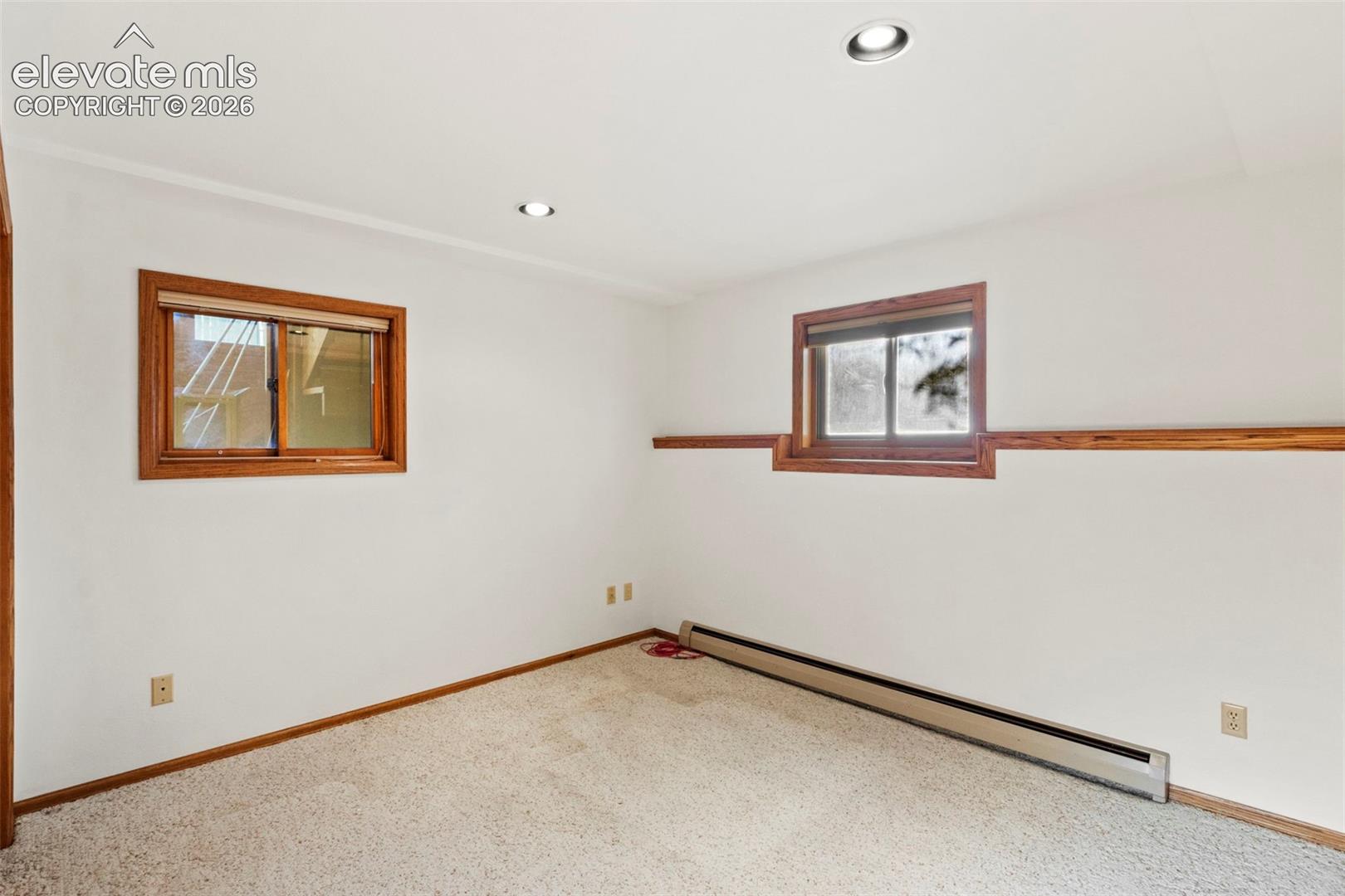 Interior room featuring neutral wall-to-wall carpeting, recessed ceiling lighting, and windows framed in natural wood trim with a horizontal wood chair rail