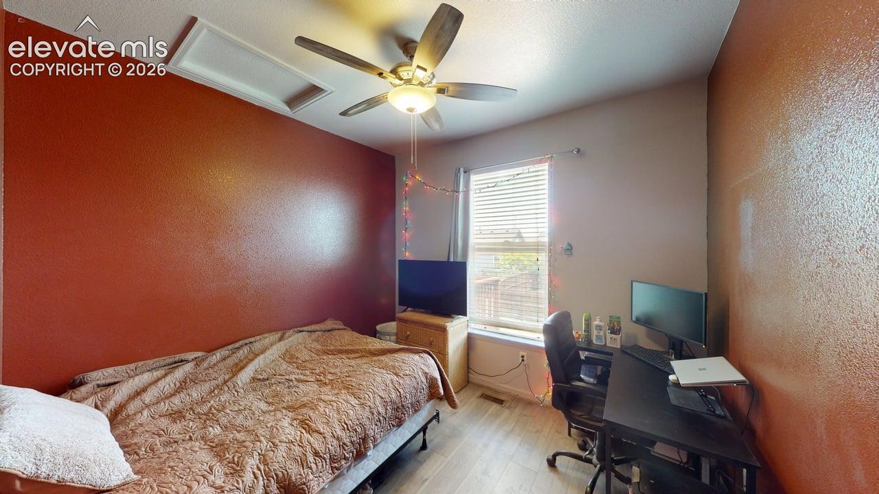 Bedroom featuring wood-finish flooring, a ceiling fan with integrated lighting, and a window with blinds