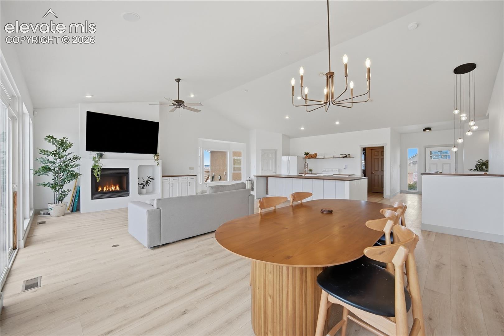 Vaulted ceilings, wood-finish flooring, built-in fireplace with custom shelving, multi-arm chandelier, and recessed lighting