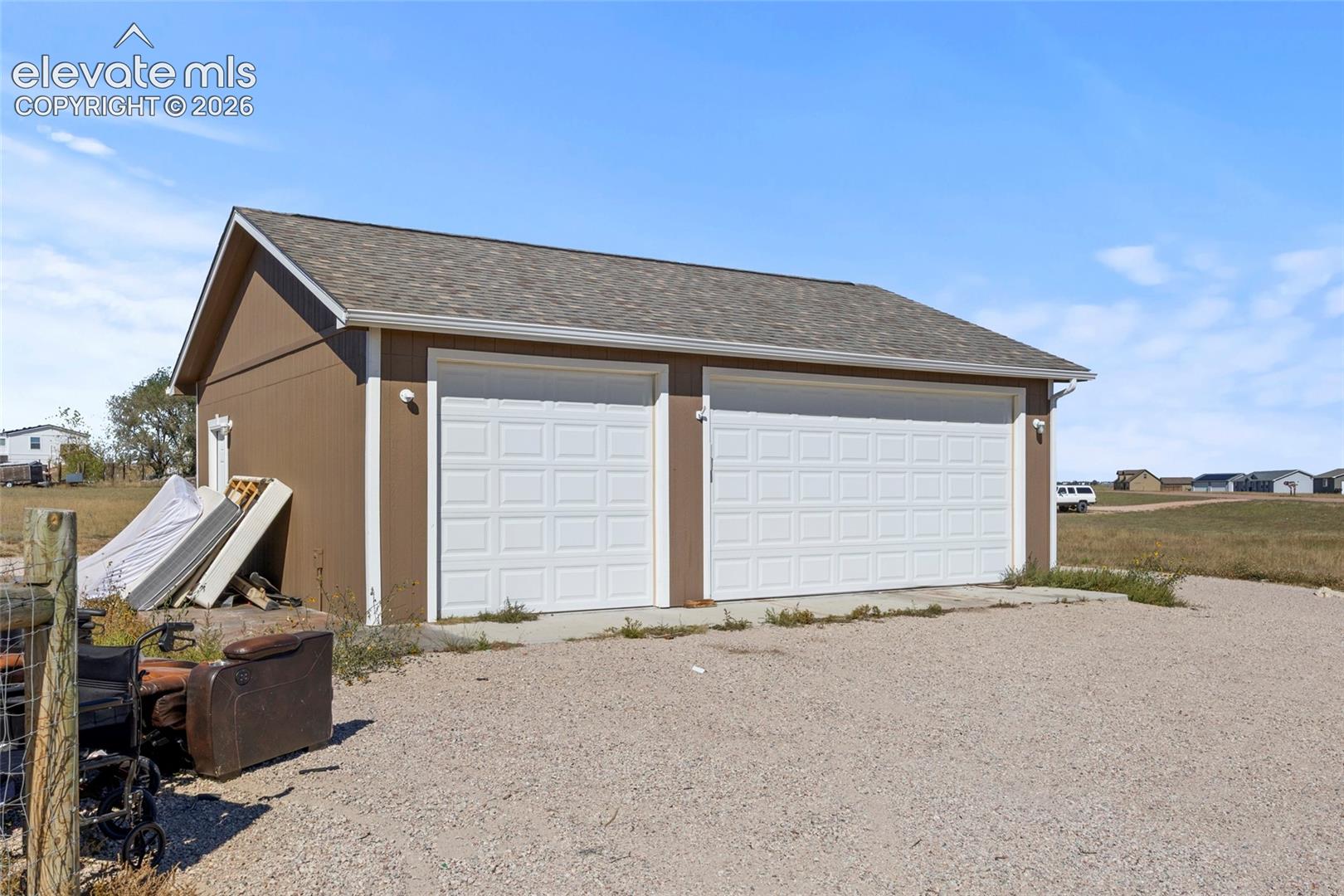 Detached two-car garage featuring shingle roofing, paneled garage doors, and exterior wall-mounted lighting
