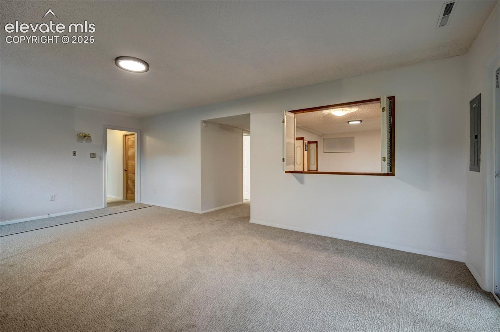 Neutral-toned wall-to-wall carpeting, flush-mount ceiling lighting, and a built-in interior pass-through window with wooden trim