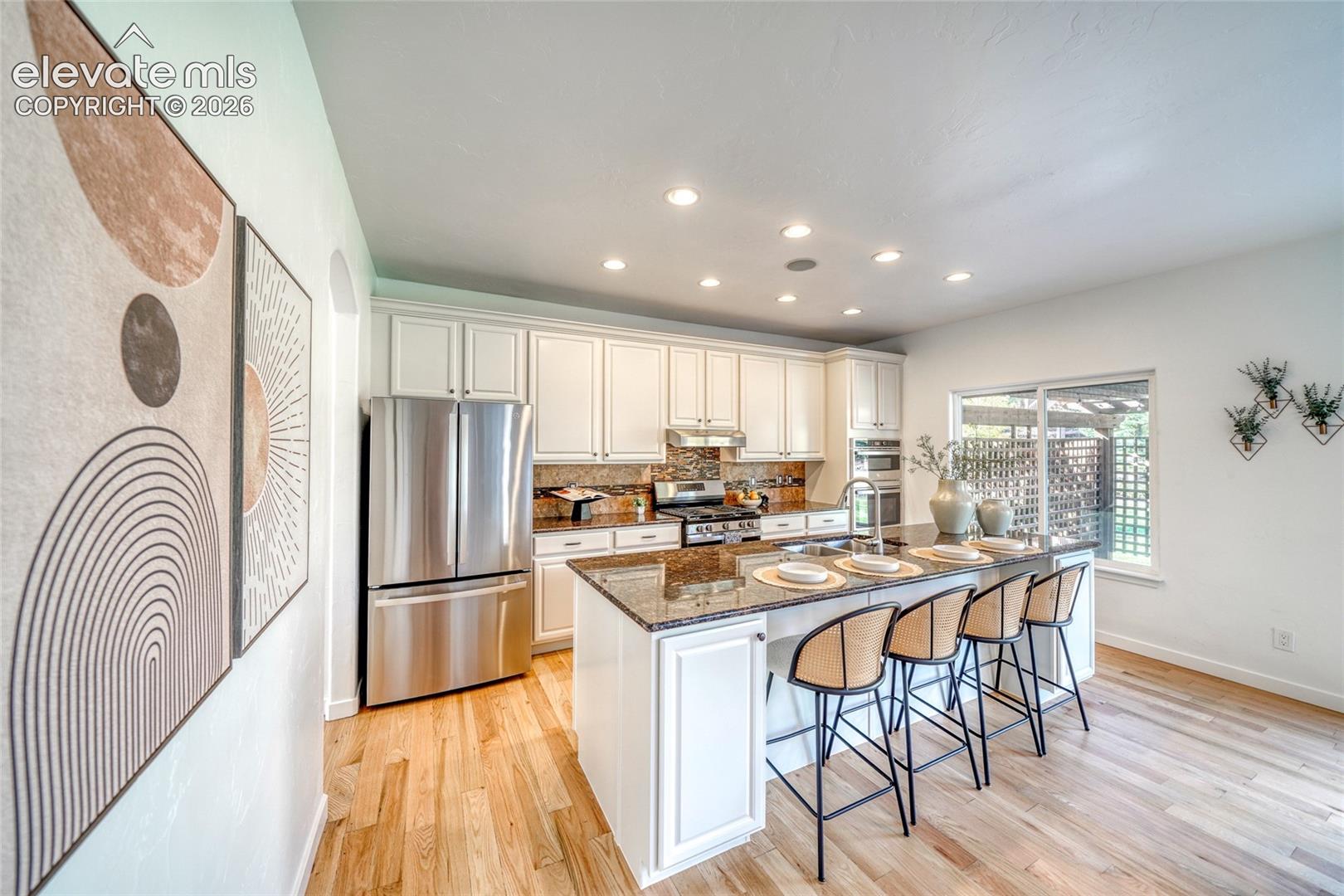 Kitchen featuring wood-finish flooring, white cabinetry, stainless steel appliances, a granite-top island with seating, and recessed lighting