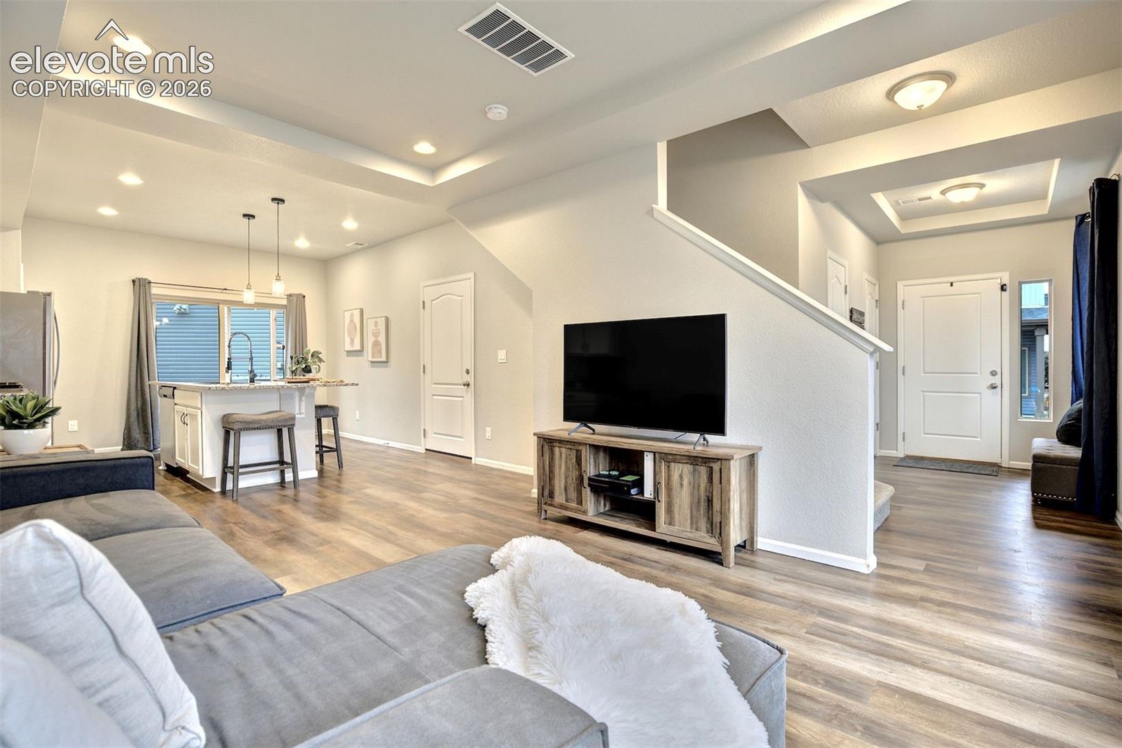 Open-concept interior featuring wood-finish flooring, tray ceilings with recessed lighting, an island kitchen with a quartz countertop, and a custom built-in half-wall partition