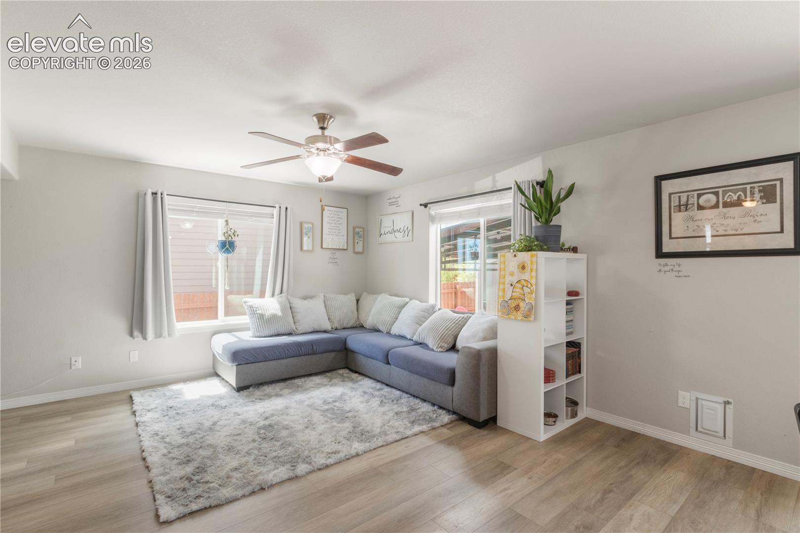 Wood-finish flooring throughout, ceiling fan with integrated lighting, large windows, sliding glass door, and a built-in shelving unit