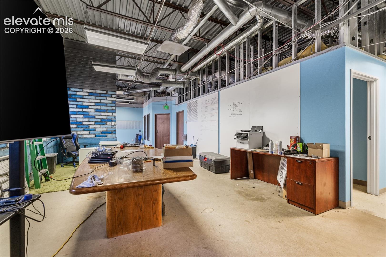 Industrial interior featuring exposed metal ceiling joists, ductwork, painted brick accent wall, and concrete flooring