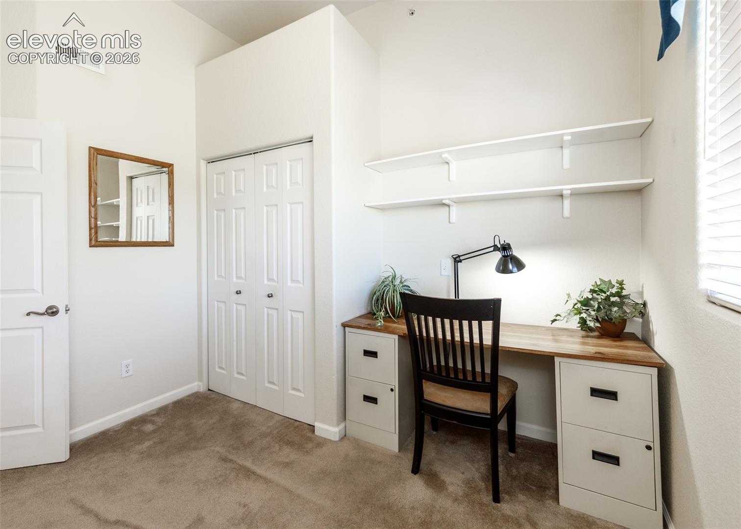 Built-in wooden desk featuring dual file cabinet pedestals, bi-fold closet doors, and wall-mounted shelving