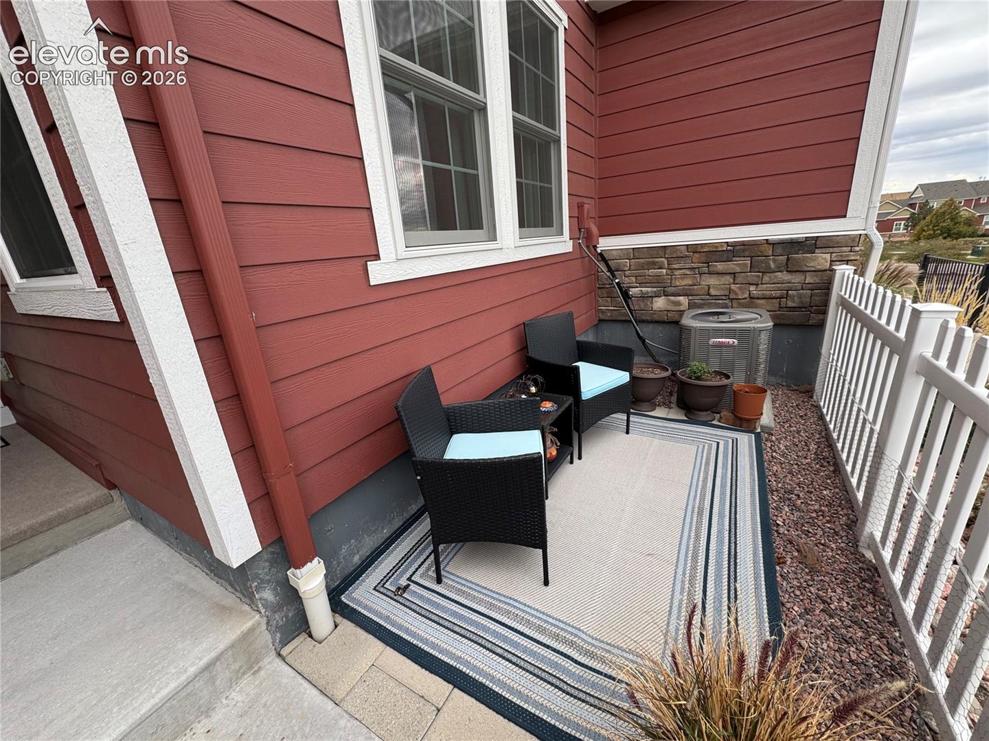 Exterior siding featuring horizontal lap boards and stone veneer accents, multi-pane windows with white trim, and a concrete patio bordered by white picket fencing