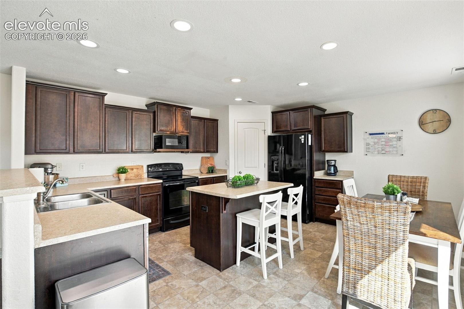 Kitchen featuring dark wood-finish cabinetry, black appliances, a central island, and recessed lighting