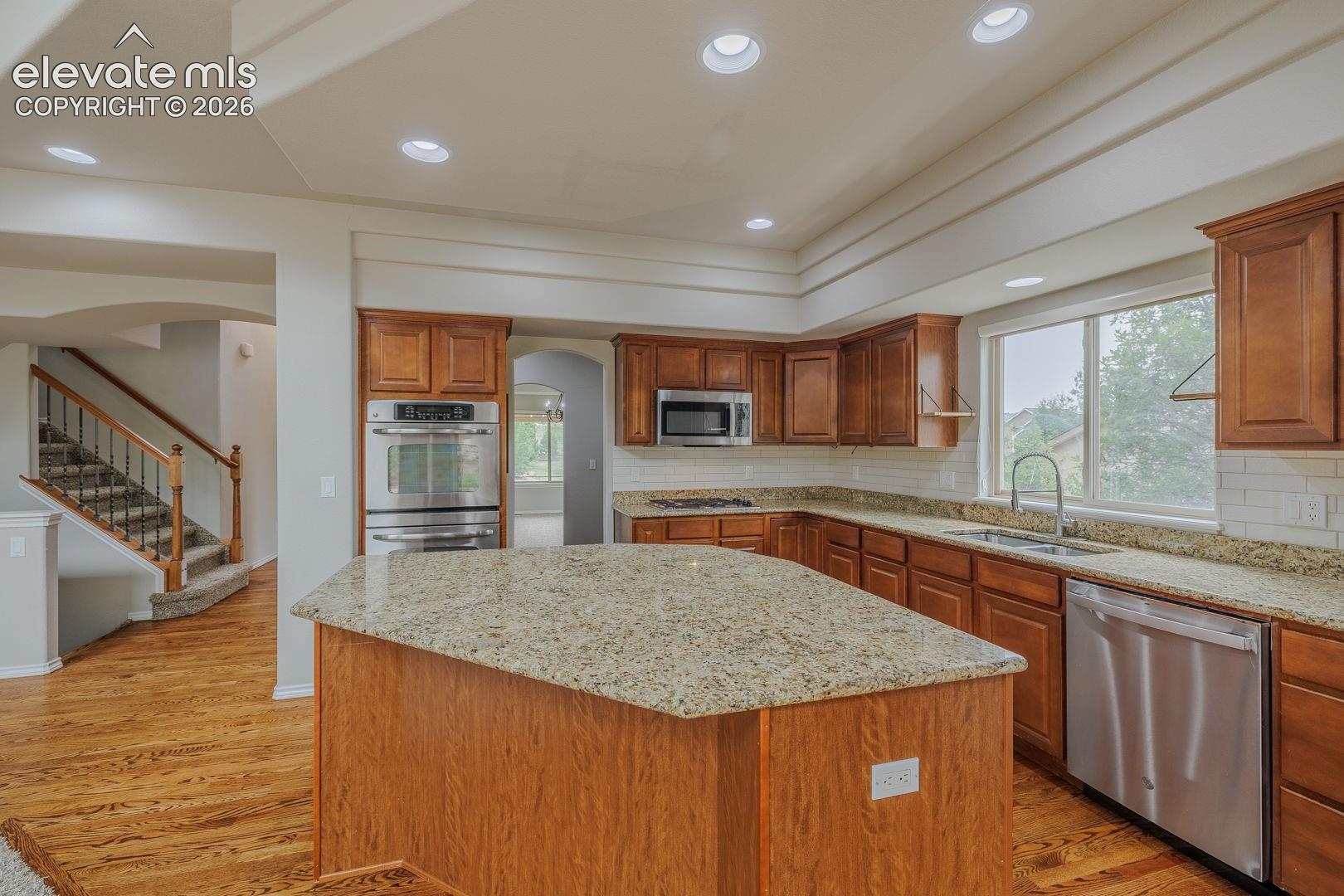 Kitchen featuring wood-finish cabinetry, granite countertops, stainless steel appliances, and a subway tile backsplash