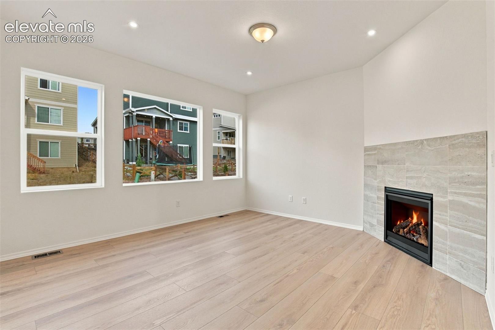 Living area featuring wood-finish flooring, recessed lighting, and a fireplace with a light-toned stone-finish surround