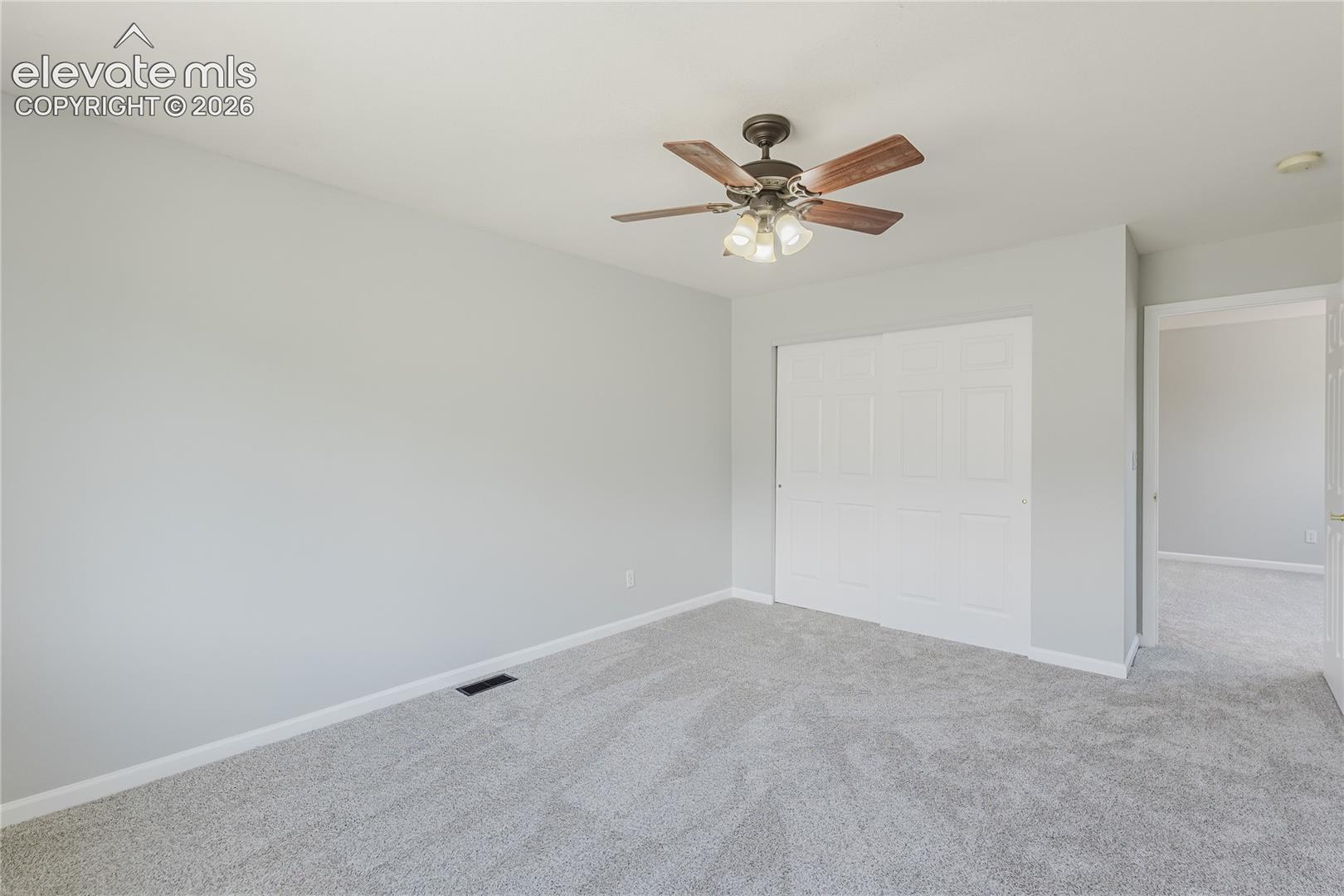 Plush carpet flooring, neutral wall paint, ceiling fan with light fixture, and closet with bi-fold doors