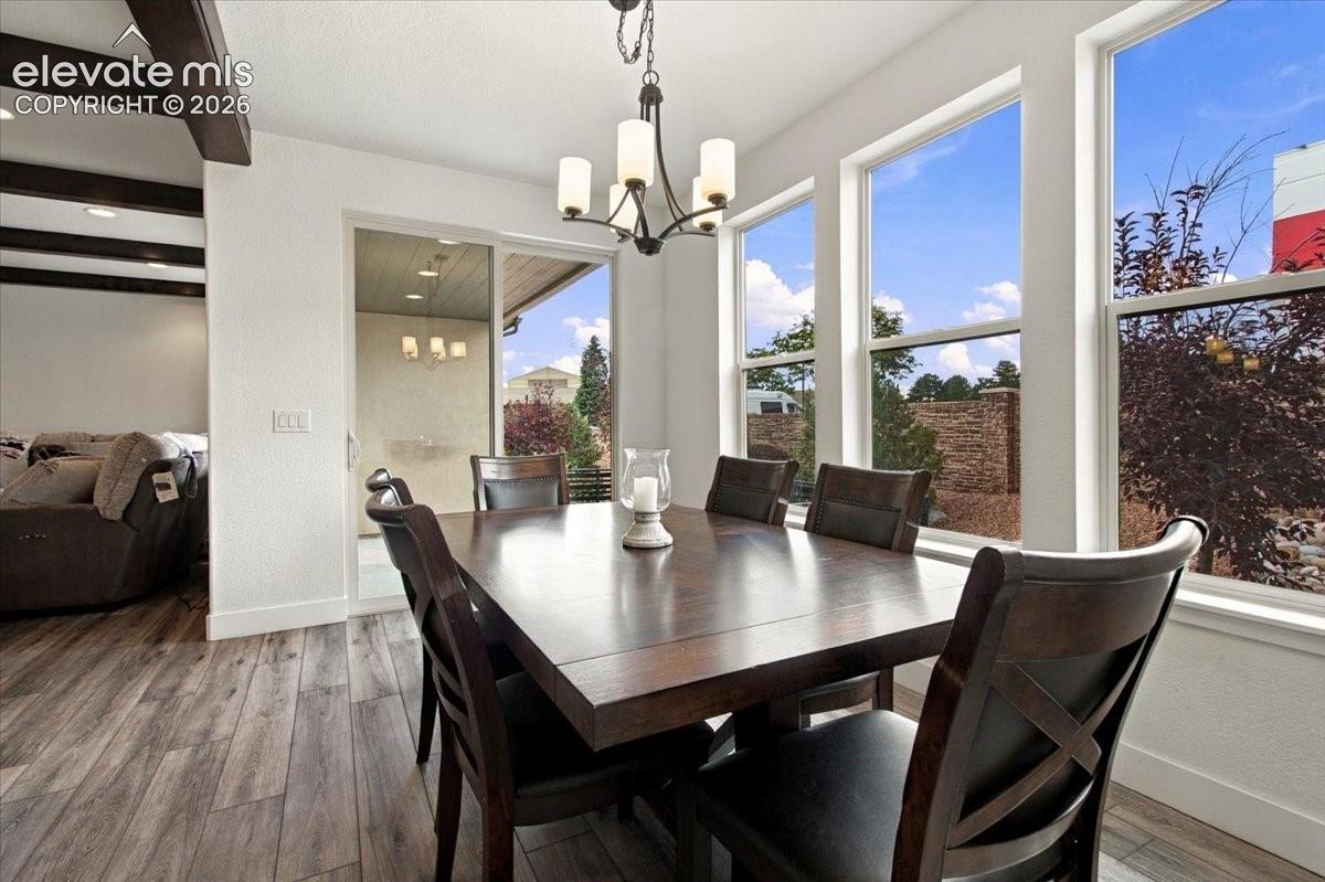 Dining area featuring wood-finish flooring, exposed ceiling beams, a multi-light chandelier, and large windows with natural lighting