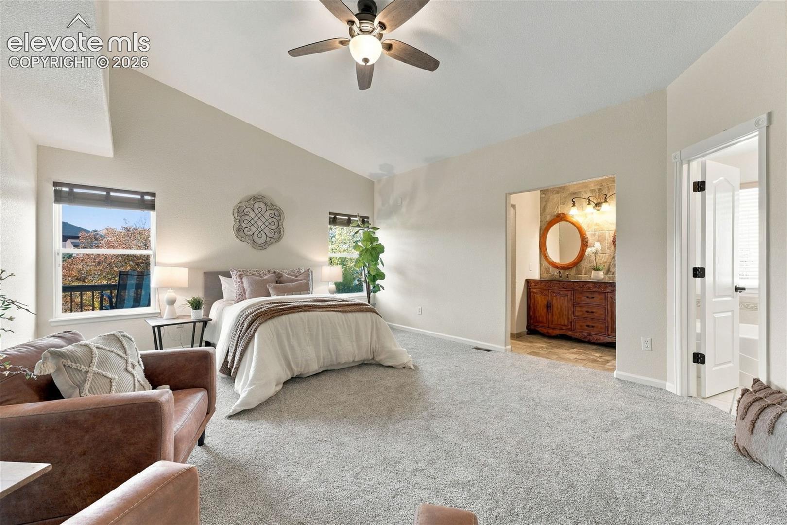 Vaulted ceiling with a central multi-blade ceiling fan, neutral wall tones, carpeted flooring, and dual window placement
