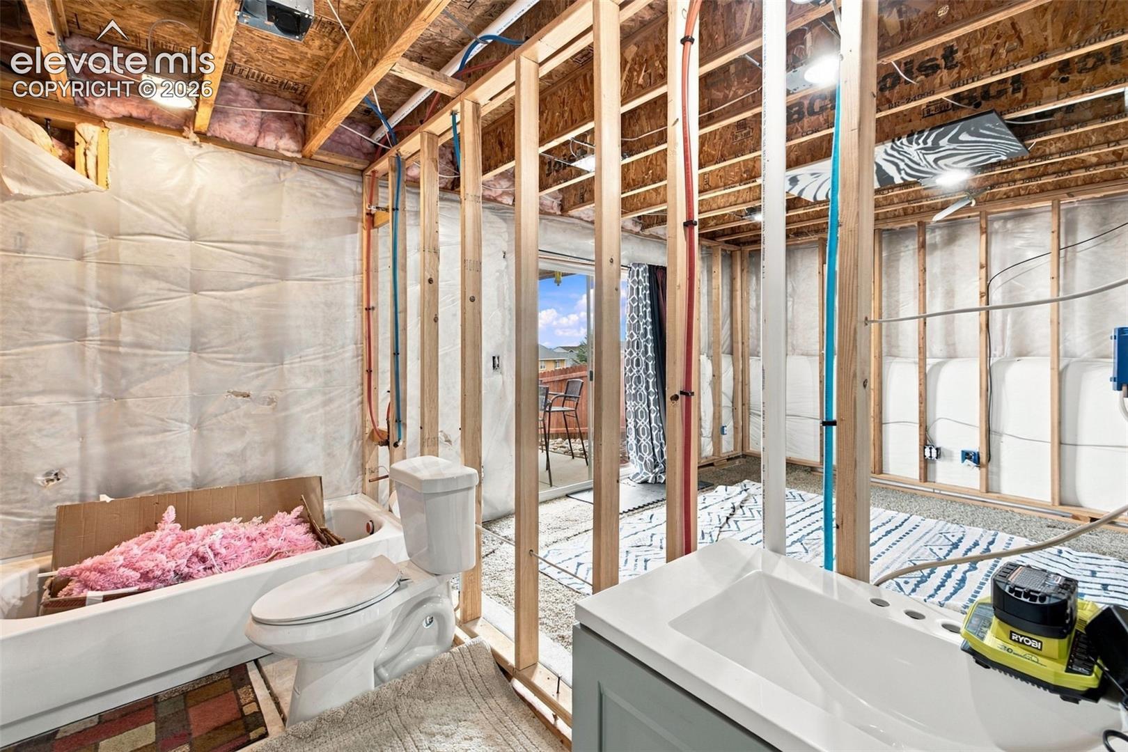 Unfinished interior space featuring exposed wood stud framing, visible plumbing lines, white fiberglass bathtub, and porcelain toilet