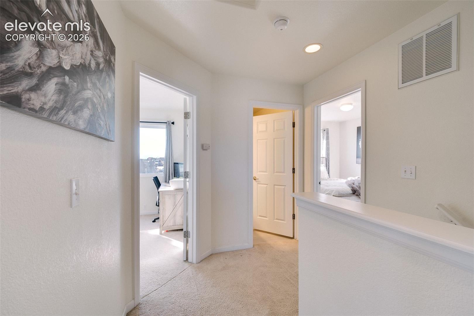 Upper-level landing with carpeted flooring, white painted walls, recessed lighting, and white paneled doors