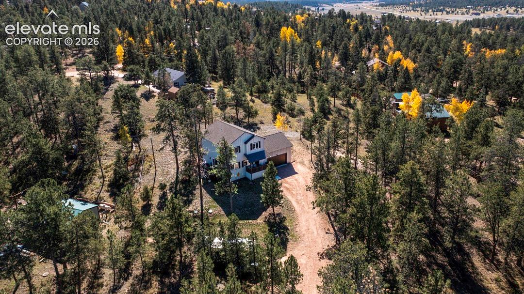Multi-level residential property featuring a light-toned exterior, an attached garage, and a sprawling lot populated with mature evergreen and deciduous trees