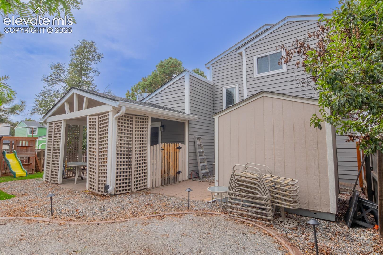 Gable-roofed pergola with lattice walls, gravel patio, and outdoor storage shed with siding