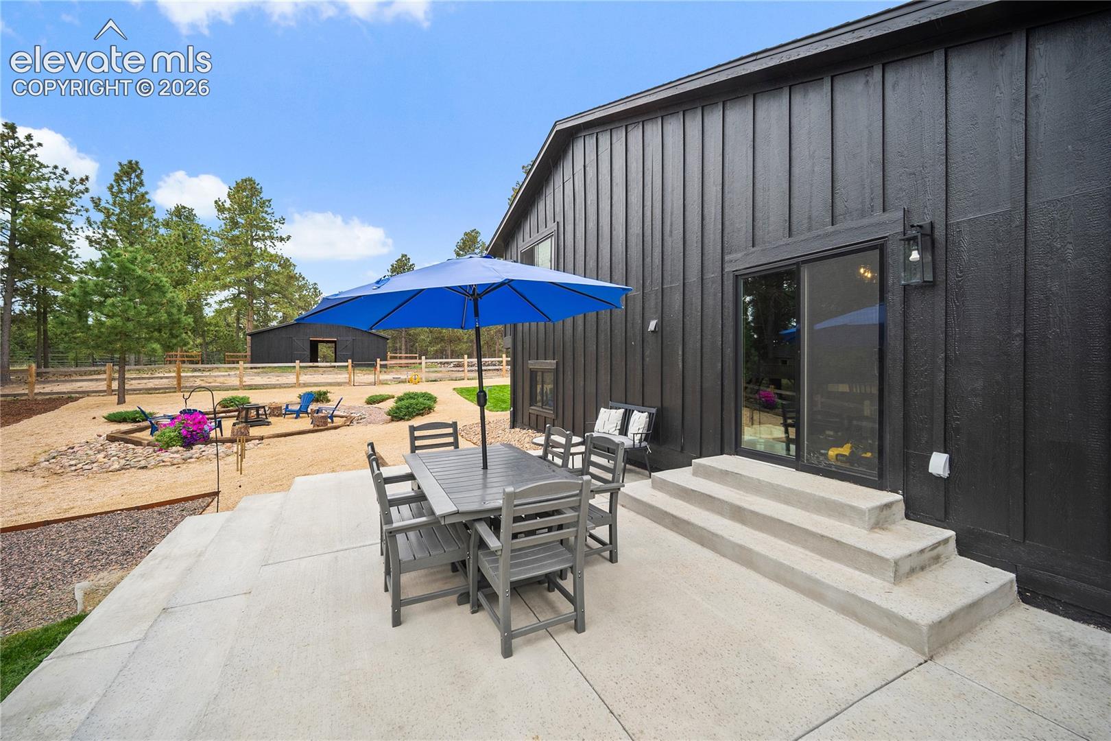 Exterior featuring black vertical siding, concrete patio, sliding glass door, and exterior sconce lighting