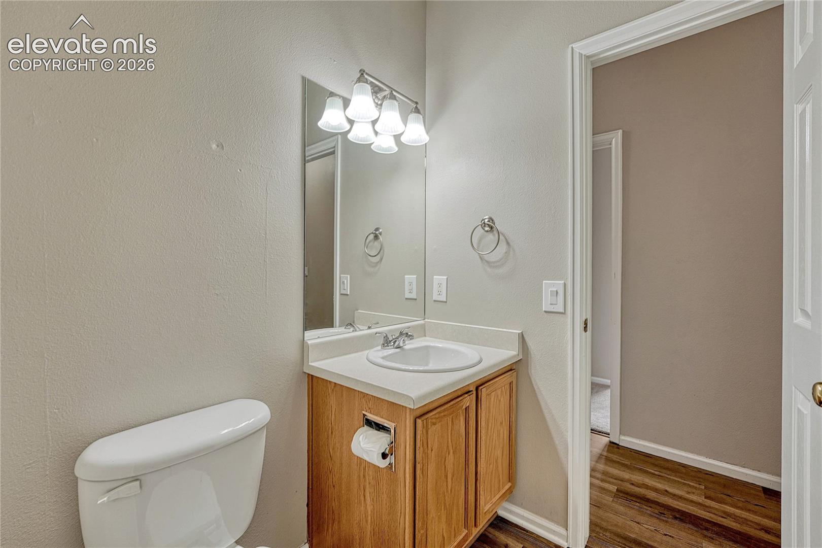 Single-sink vanity with wood cabinetry, solid-surface countertop, integrated basin, wall-mounted mirror, and five-light vanity fixture