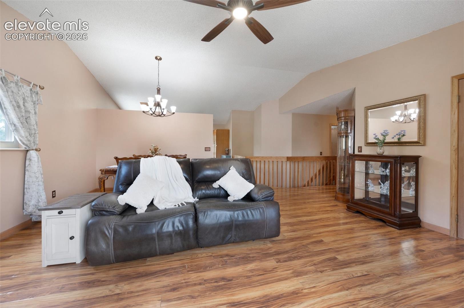 Living area featuring vaulted ceiling, ceiling fan, a chandelier, light wood-type flooring, and baseboards