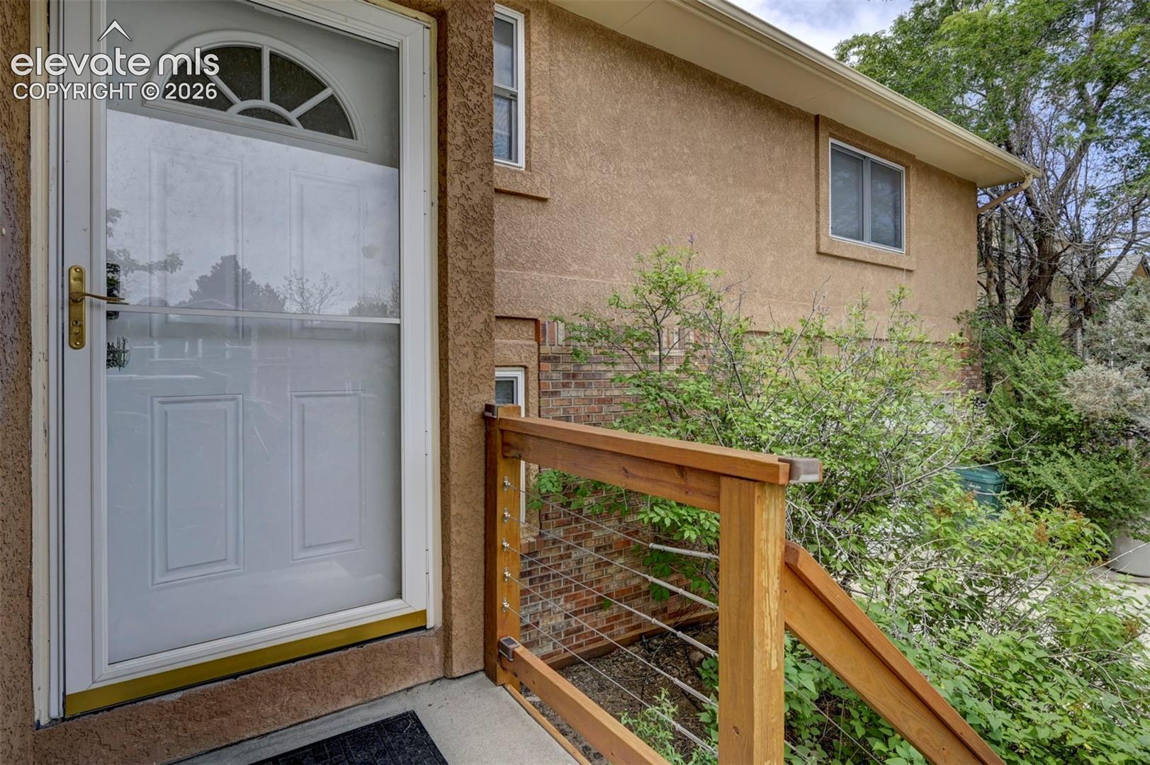 Entryway featuring a white storm door with an arched window, wood railing with cable infill, and stucco exterior