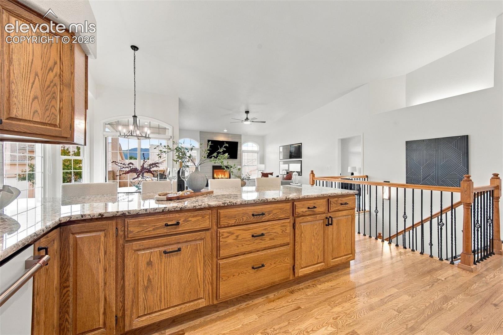 Kitchen featuring an oversized stone-topped island, light wood-finish cabinetry, hard surface flooring, and a staircase with wood railing and metal balusters