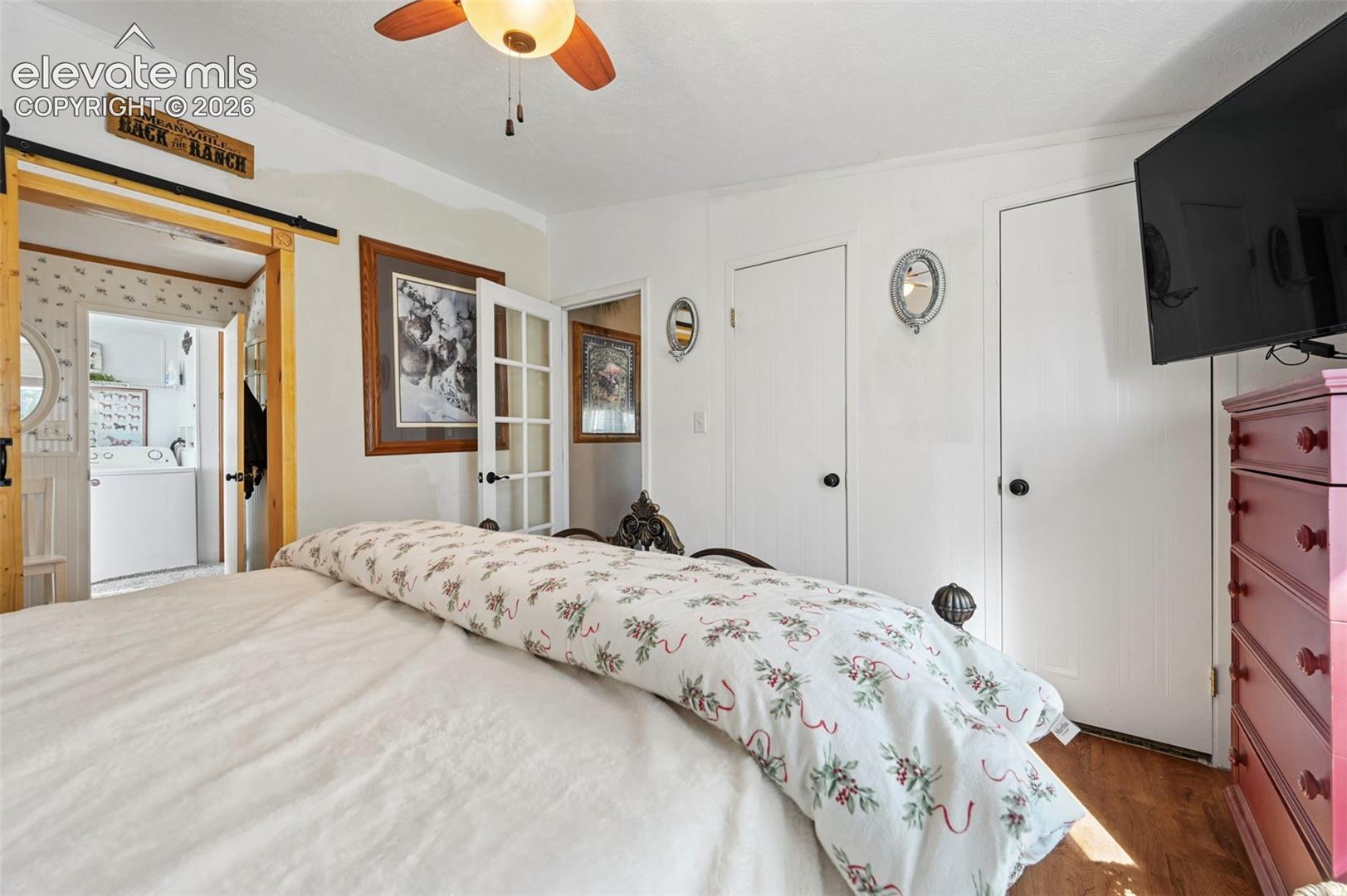 Wood-finish flooring, ceiling fan with light fixture, sliding barn-style door, and multi-pane glass door, double closets
