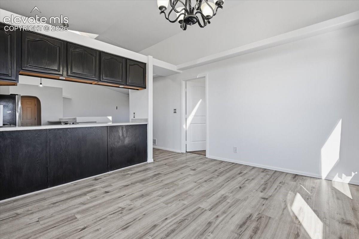 Open interior featuring wood-finish flooring, dark-toned cabinetry, a pass-through counter, and a multi-arm chandelier