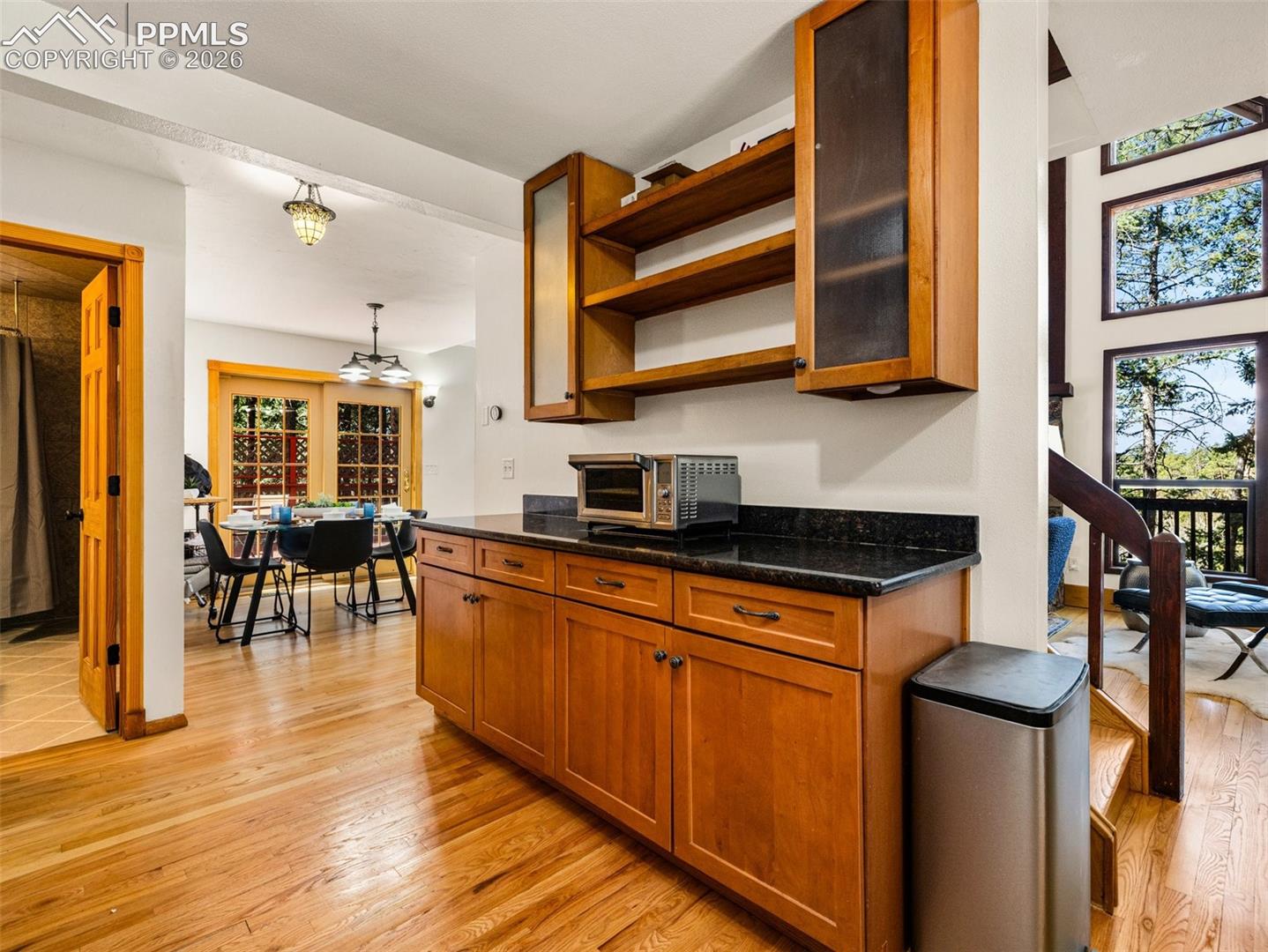 Kitchen featuring wood finish cabinets, open shelves, light wood finished floors, dark stone counters, and glass insert cabinets
