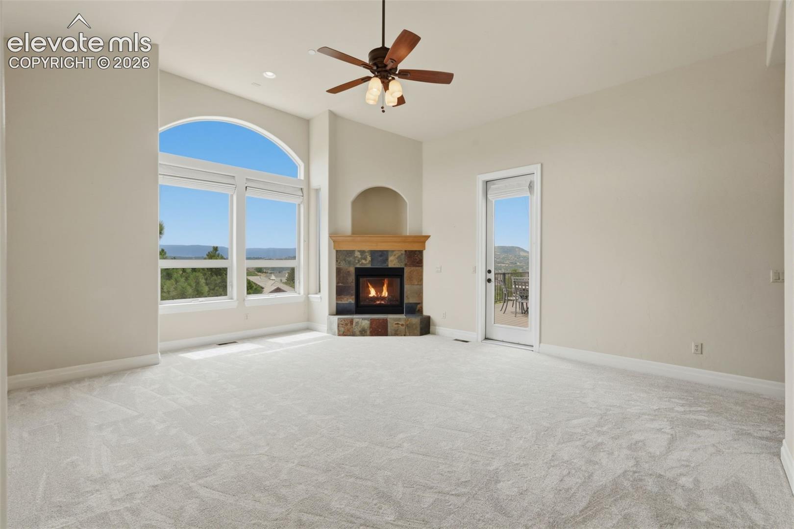 Spacious interior with vaulted ceilings, a corner stone fireplace, and a ceiling fan