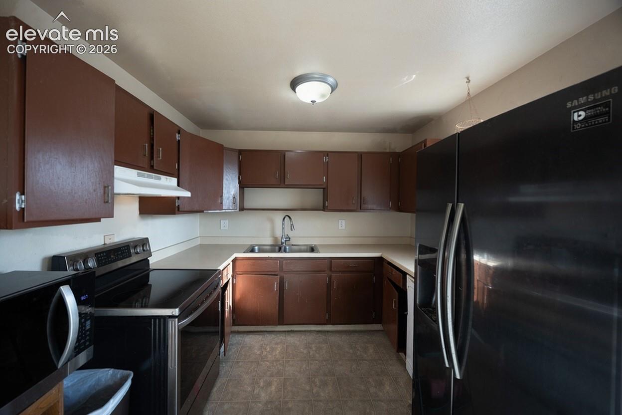 Kitchen featuring wood-finish cabinetry, solid surface countertops, a stainless steel sink with a gooseneck faucet, and a black Samsung refrigerator