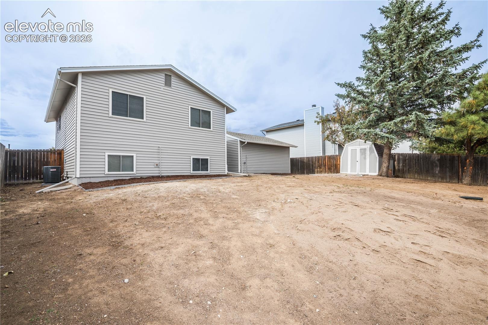 Exterior featuring light gray horizontal siding, a fenced backyard, detached storage shed, and mature evergreen trees