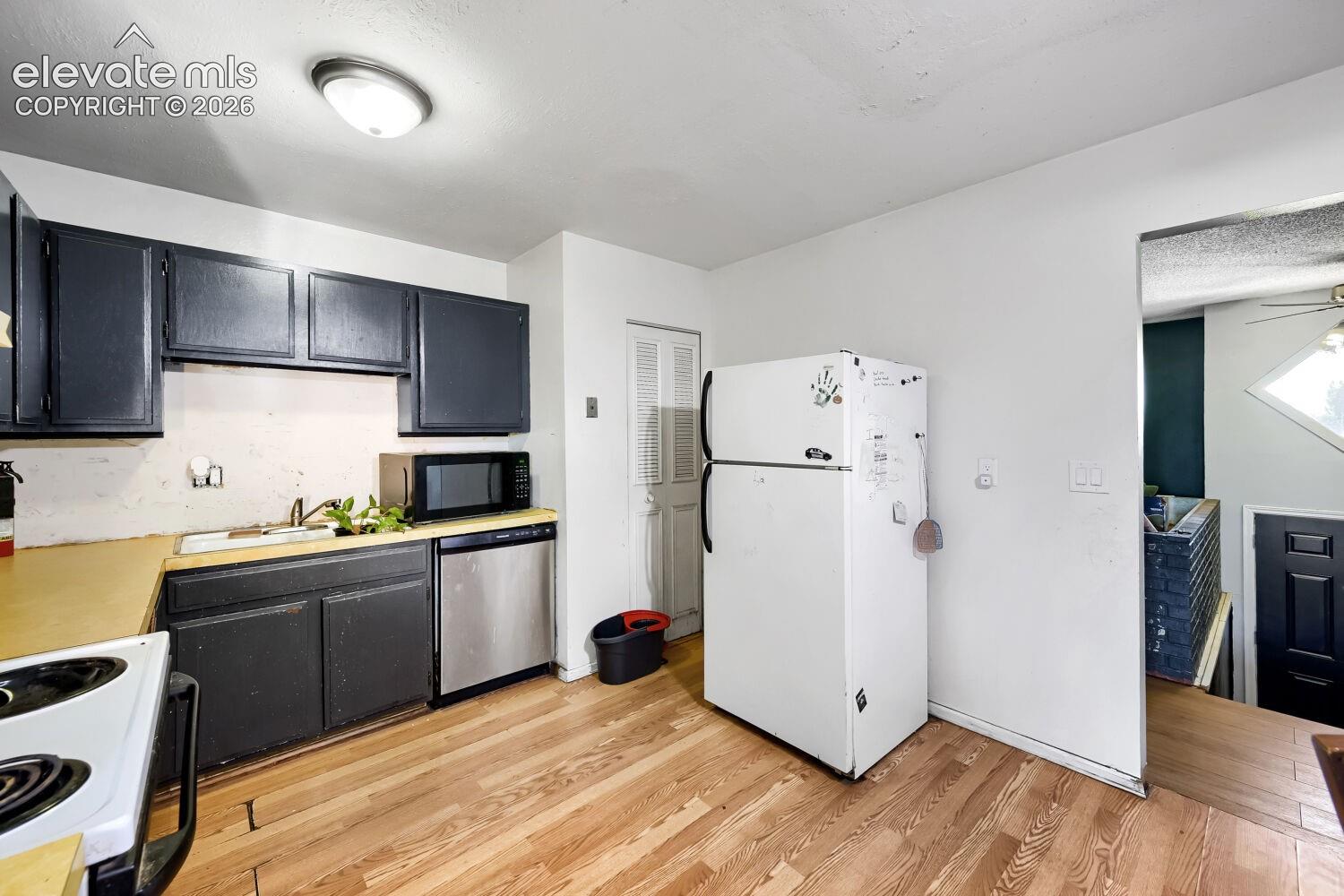 Kitchen featuring wood-finish flooring, dark cabinetry, and a stainless steel dishwasher