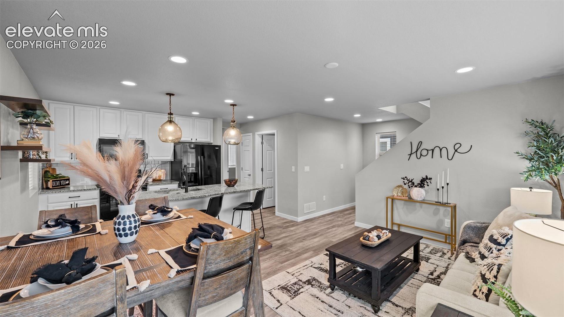 Open-concept kitchen featuring white cabinetry, stone-finish countertops, recessed lighting, glass pendant lights, and wood-finish flooring