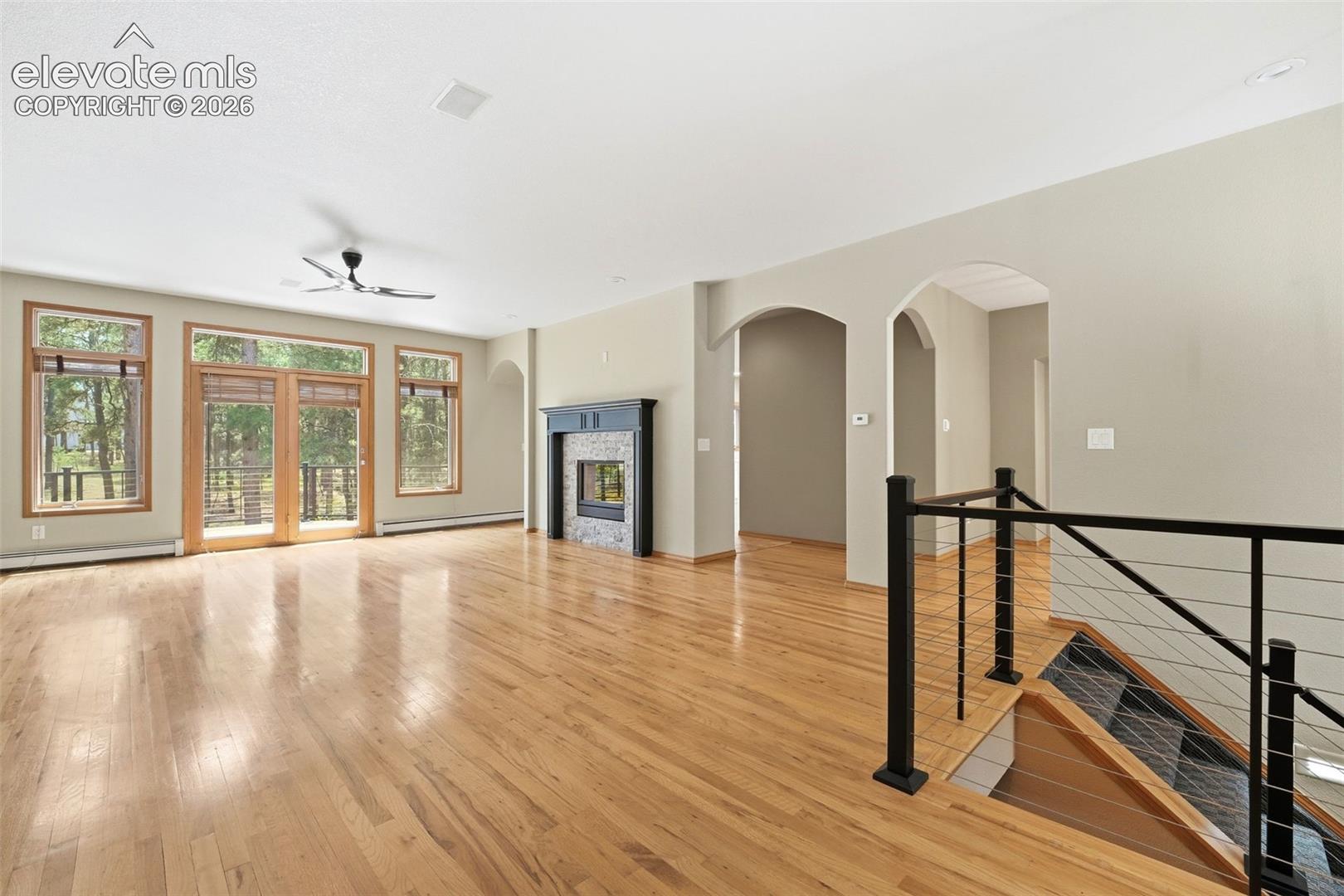 Open-concept living area featuring wood-finish flooring, a contemporary ceiling fan, and a fireplace with a stone surround