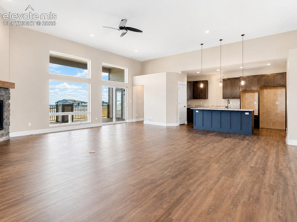 Open-concept living area featuring wood-finish flooring, a stone-faced fireplace with a wood mantle, and a modern ceiling fan