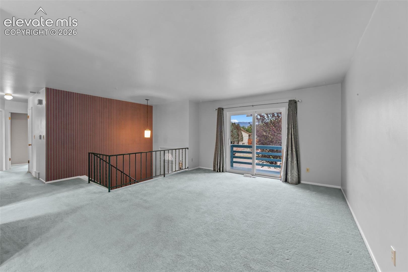 Sliding glass door, light blue carpeting, horizontal wood panel accent wall, pendant lighting, black metal railing