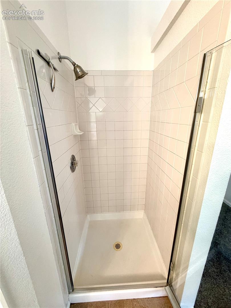 Walk-in shower featuring white subway tile, decorative accent tiles, a single shower head, a chrome temperature control handle, and a clear glass enclosure