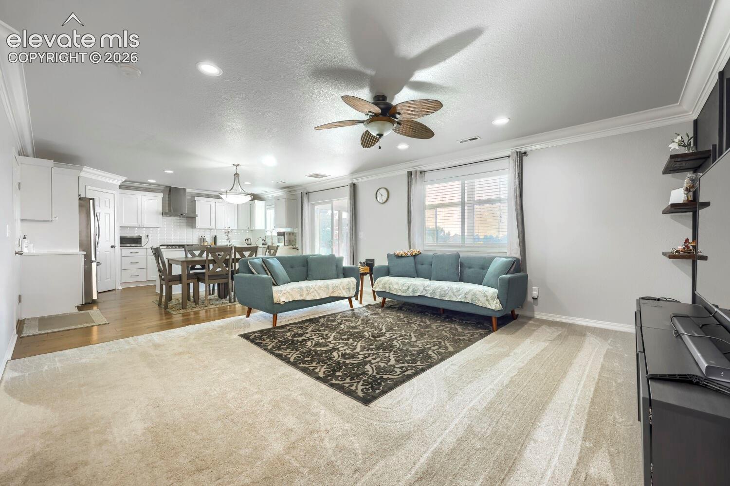 Open-concept living space featuring wood-finish flooring, recessed lighting, a ceiling fan with integrated lighting, crown molding, and built-in wall shelving