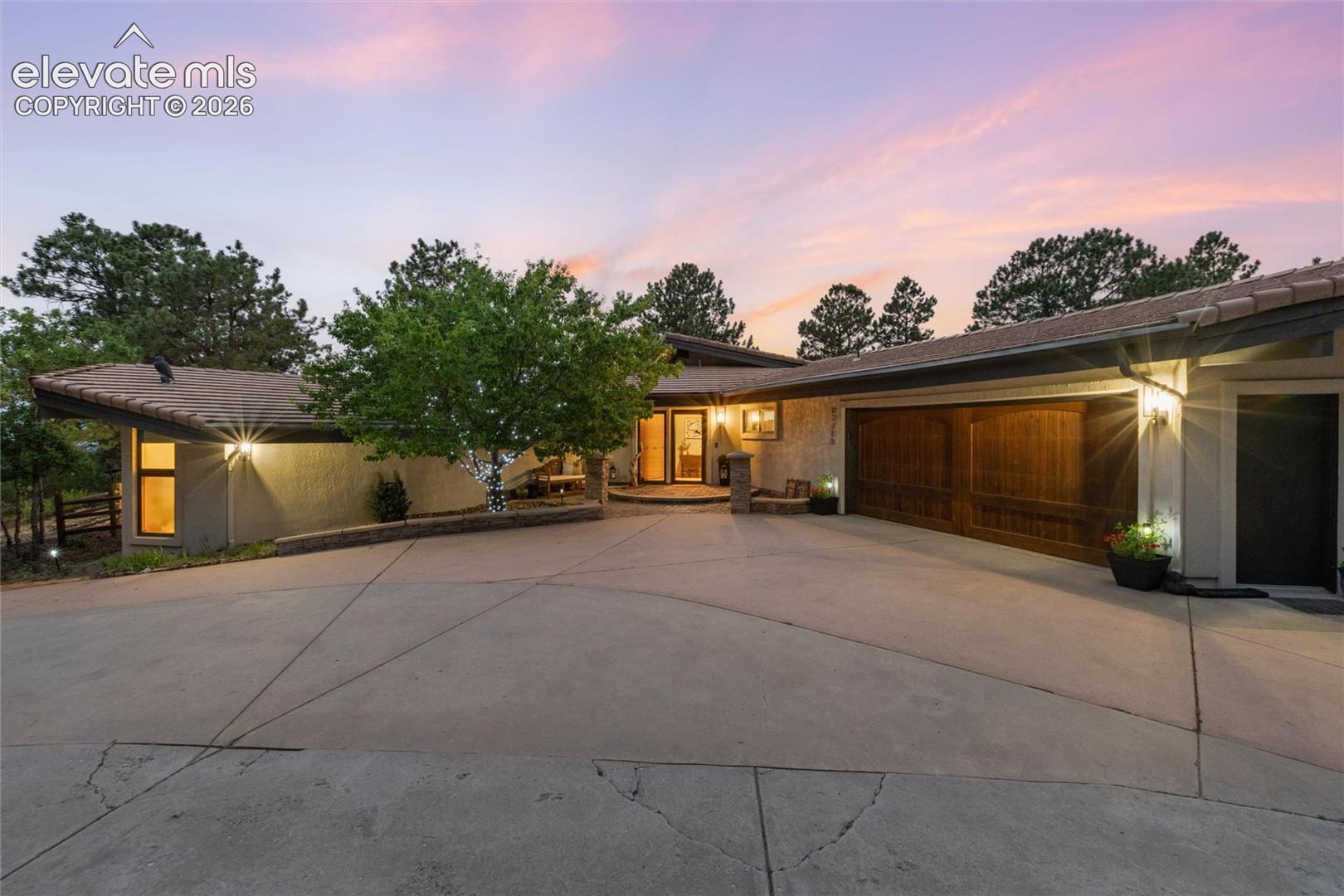 Contemporary ranch-style residence featuring a prominent two-car wood-paneled garage door, a concrete driveway, and exterior wall sconce lighting