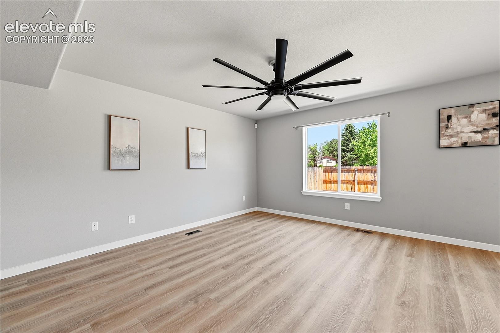 Spacious room featuring wood-finish flooring, a large window, a modern black ceiling fan, and light gray walls